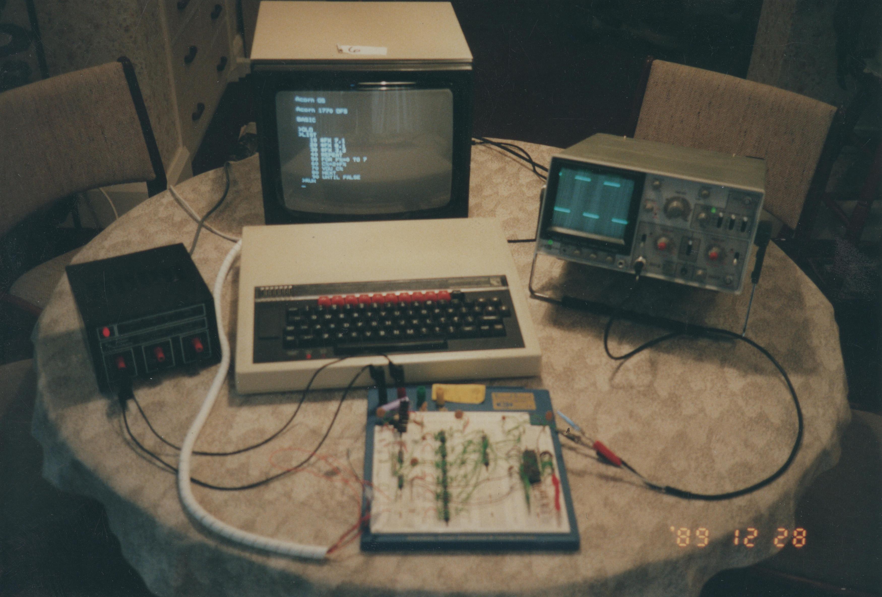 A BBC Microcomputer, oscilloscope and breadboard with circuitry on a round table.